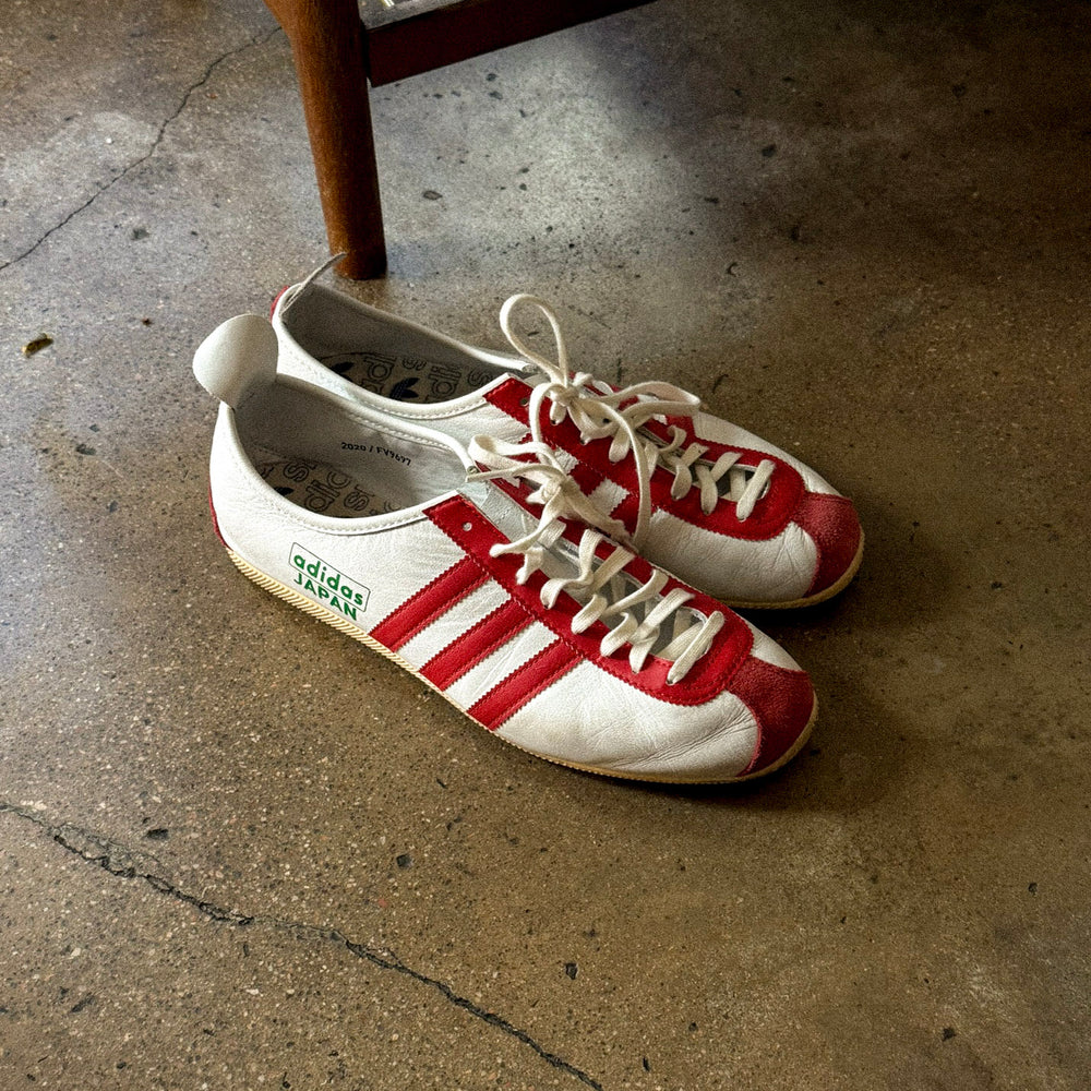 Japanese adidas sitting on concrete floor next to wooden stool 