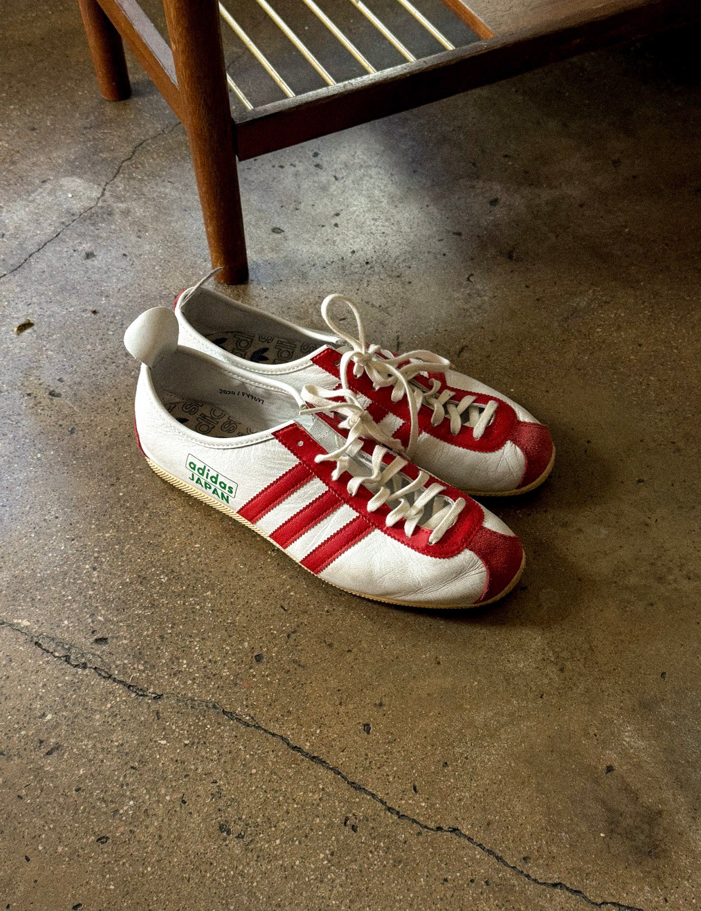 Japanese adidas sitting on concrete floor next to wooden stool 