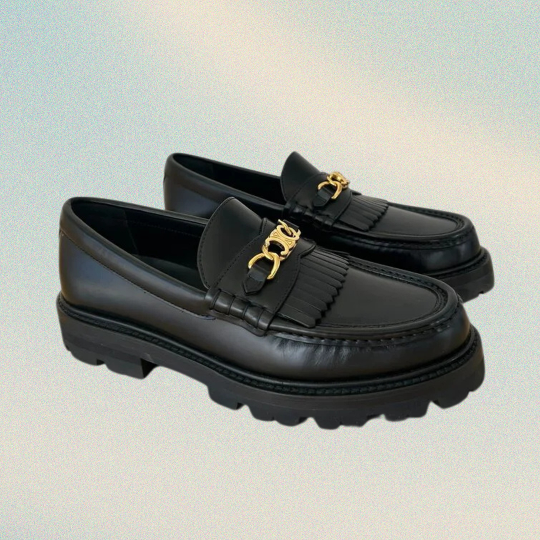 Black loafers with gold accents on a gradient background