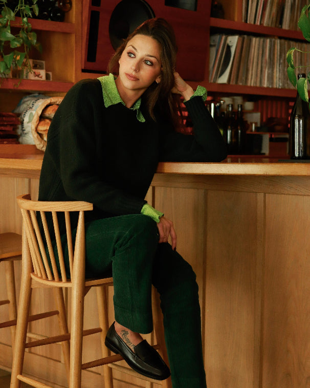 Woman sitting on a bar stool in a cozy room with wooden furniture and decor.