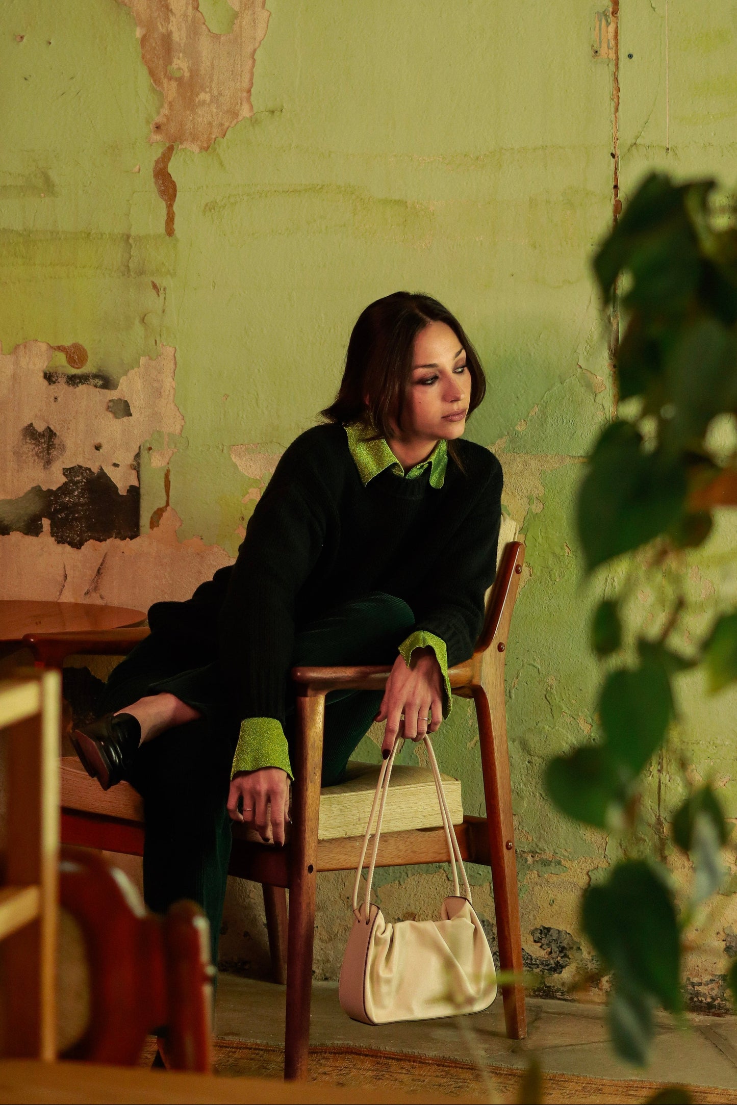 Woman sitting on a chair against a green wall with peeling paint