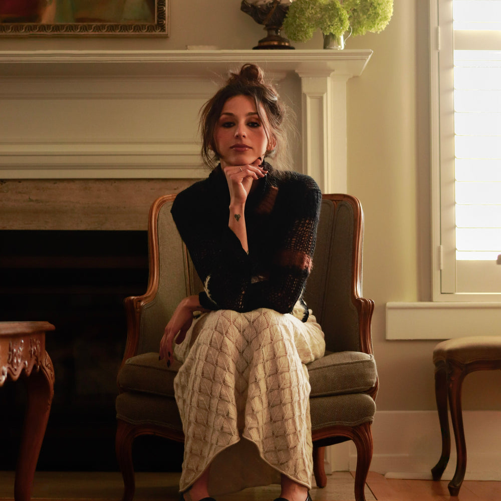 Woman sitting in a chair in a room with a fireplace and decorative items.