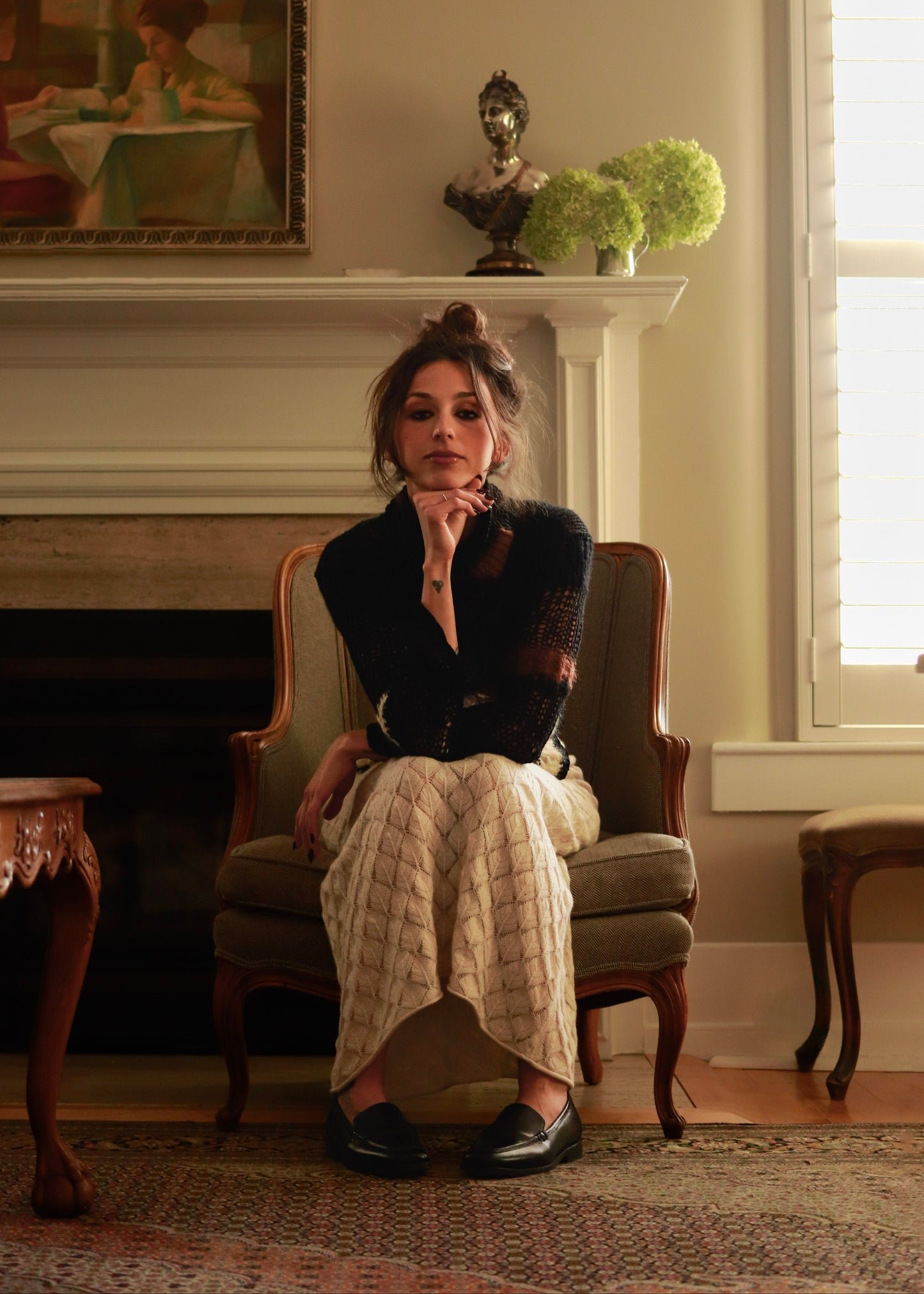 Woman sitting in a chair in a room with a fireplace and decorative items.