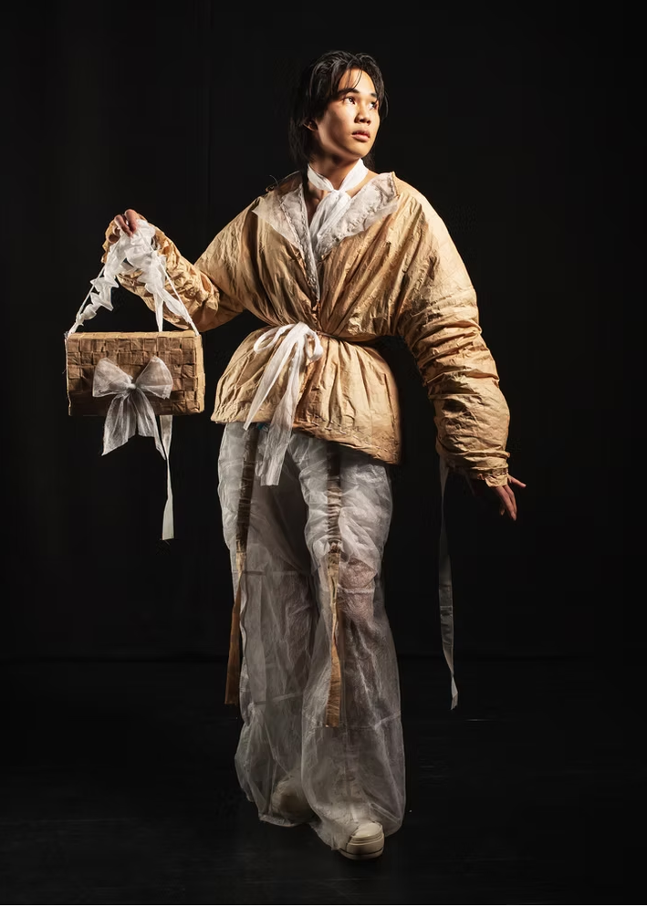 Person in historical costume holding a basket against a black background
