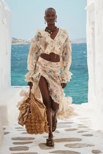 Woman in a floral dress standing on a stone path with ocean and blue sky in the background