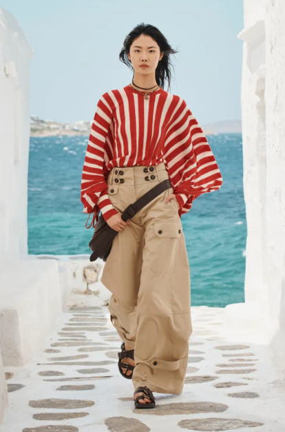 Person wearing a red and white striped sweater and beige pants standing on a stone path with ocean view.