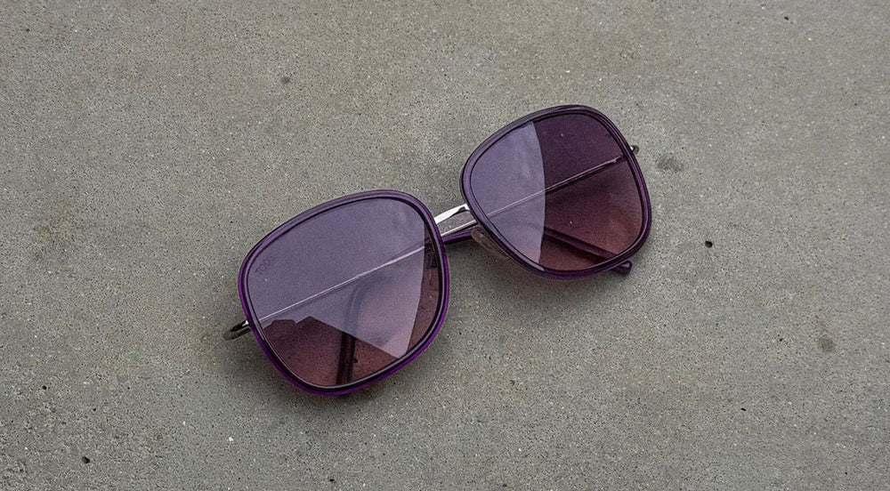 Purple sunglasses on a gray concrete surface
